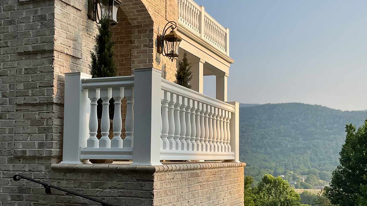 Elegant brick balcony with white balustrades and decorative lanterns, overlooking a scenic mountain landscape under a hazy sky.