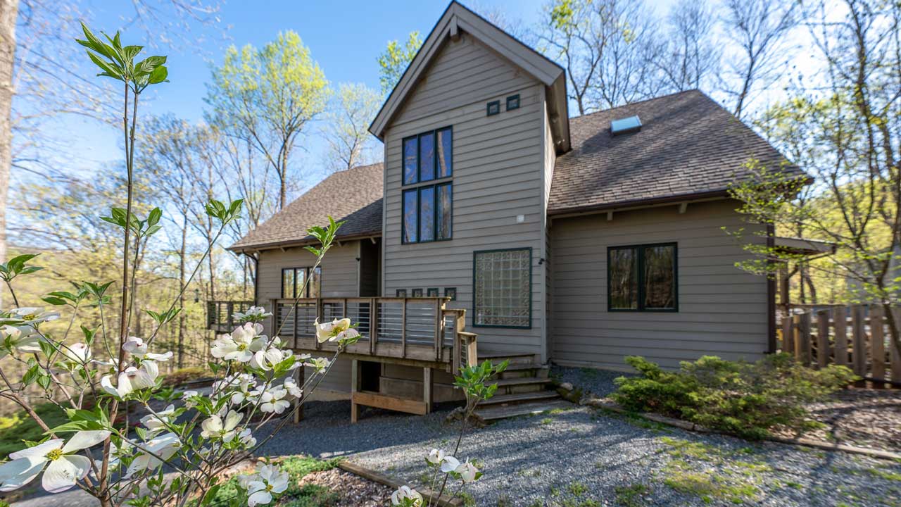 Secluded retreat property in Nelson County, VA, featuring a contemporary wood-sided home with large windows, a wraparound deck, and a tranquil wooded setting, perfect for relaxation and nature escapes.